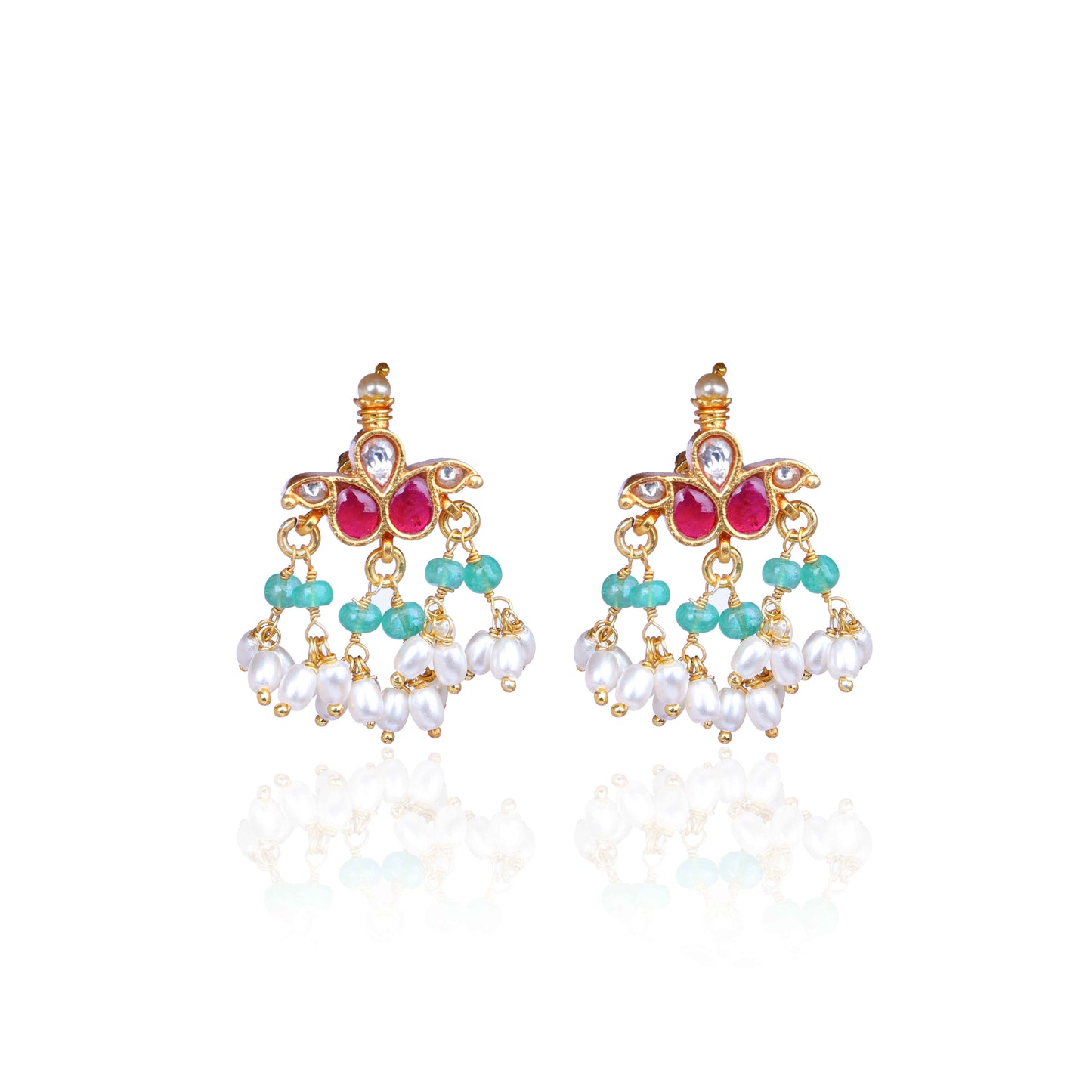 A pair of gold-plated Kundan chandelier earrings featuring ruby-red stones, emerald-green beads, and dangling freshwater pearls, displayed on a branch against a neutral background.