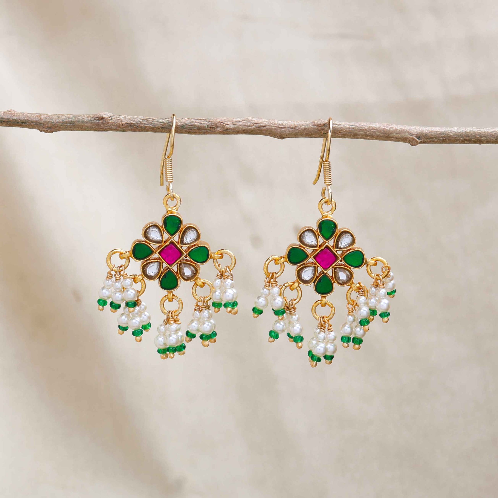 Gold-plated Kundan earrings with a floral motif, pink, green, and white gemstones, and dangling pearl clusters, worn by a model.