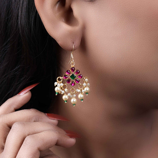 Gold-plated floral chandelier earrings with red and green gemstones, pearl drop accents, and intricate detailing, perfect for ethnic and festive wear.