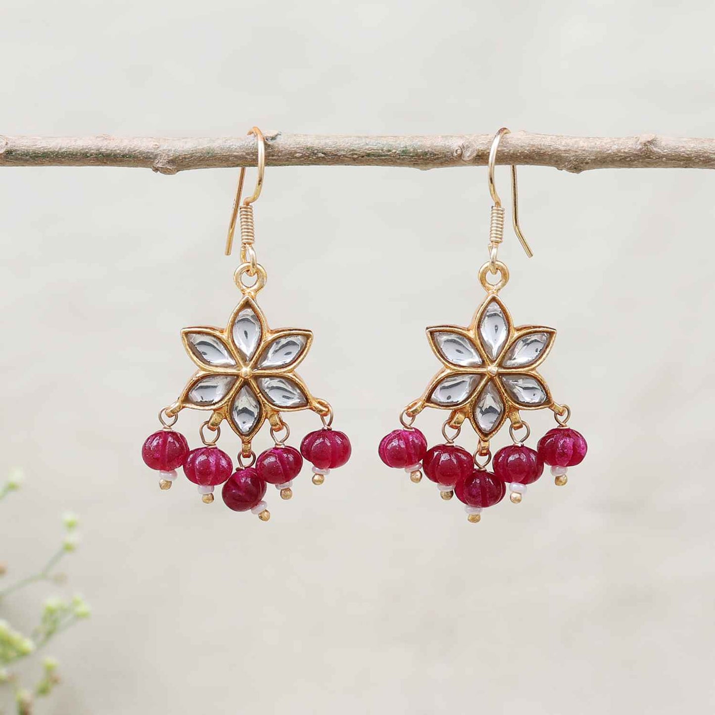 Gold-plated floral Kundan earrings featuring a six-petal design with clear gemstones and dangling red beads, elegantly worn by a model.