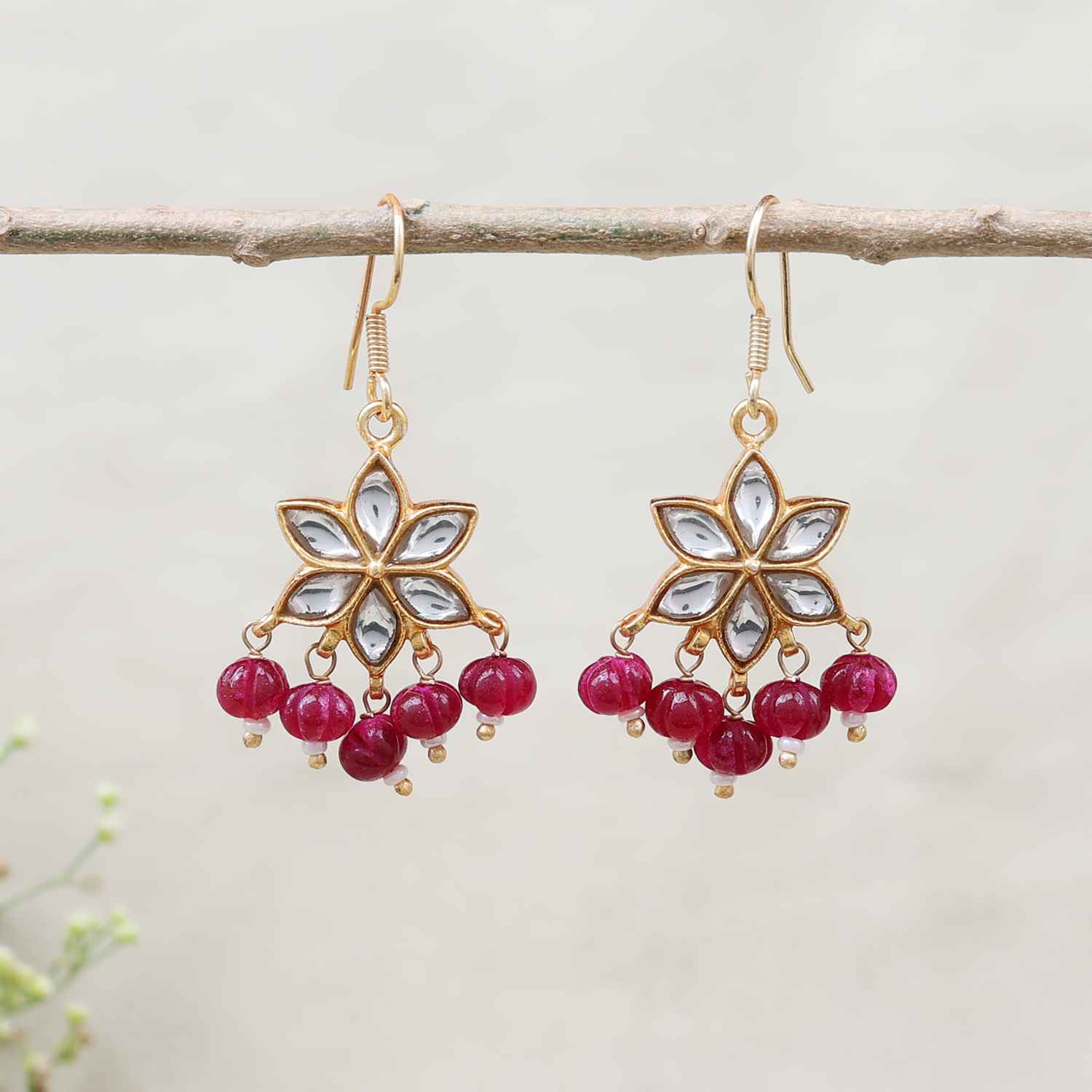Gold-plated floral Kundan earrings featuring a six-petal design with clear gemstones and dangling red beads, elegantly worn by a model.
