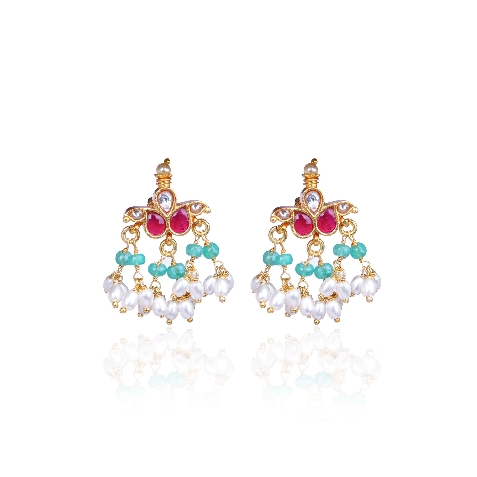 A pair of gold-plated Kundan chandelier earrings featuring ruby-red stones, emerald-green beads, and dangling freshwater pearls, displayed on a branch against a neutral background.
