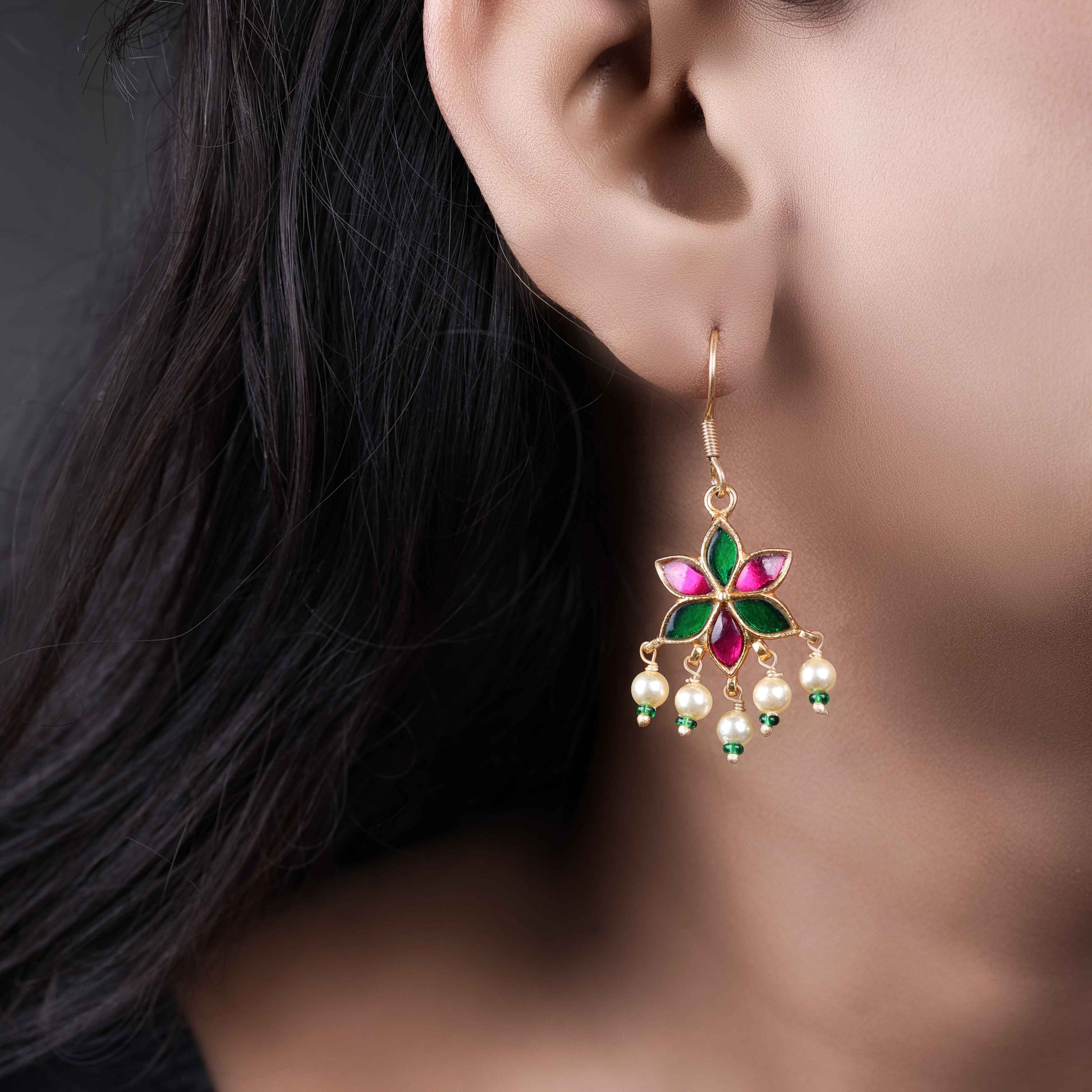 A gold-plated floral drop earring with pink and green enamel petals, featuring dangling freshwater pearls and green bead accents, worn by a model.