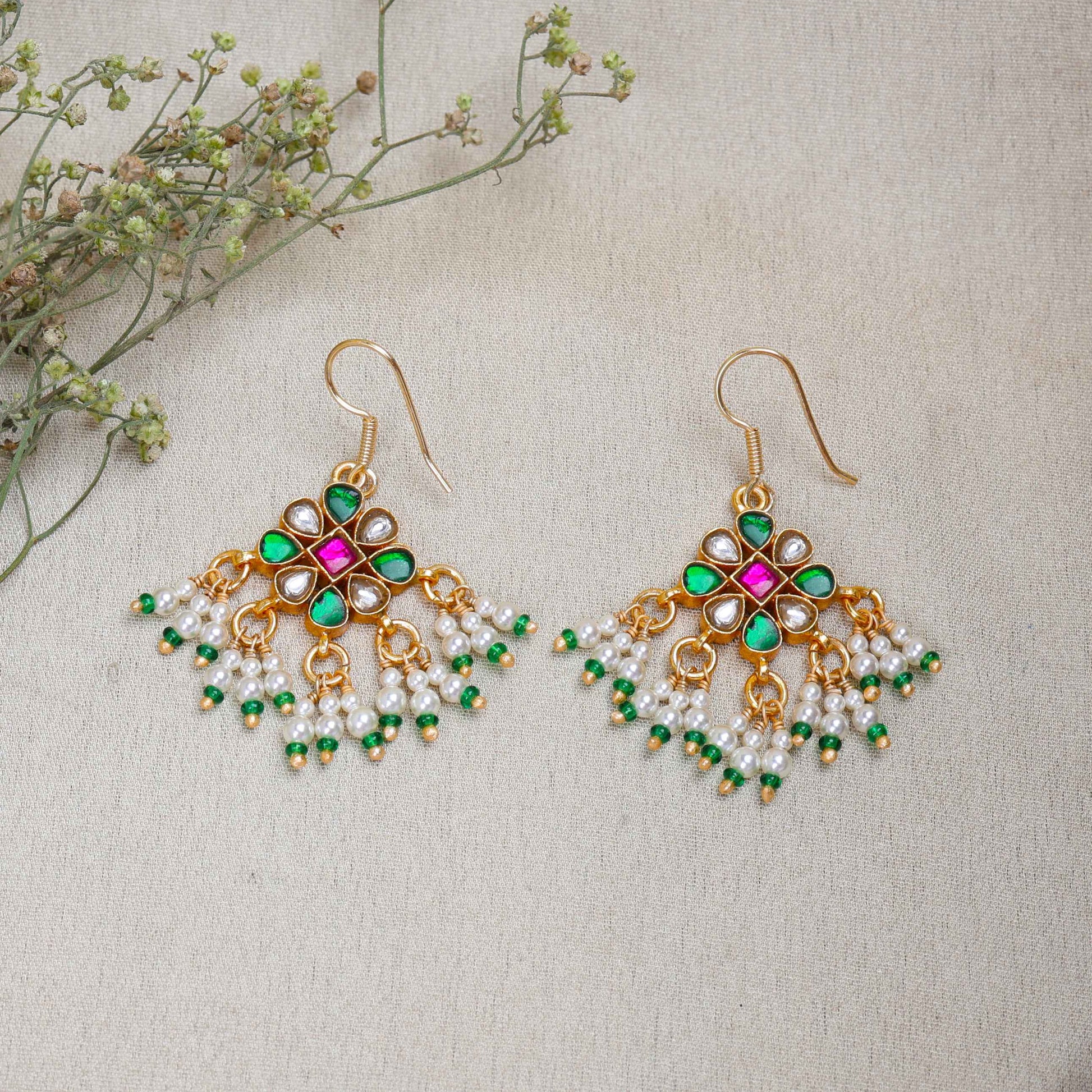 Gold-plated Kundan earrings with a floral motif, pink, green, and white gemstones, and dangling pearl clusters, worn by a model.