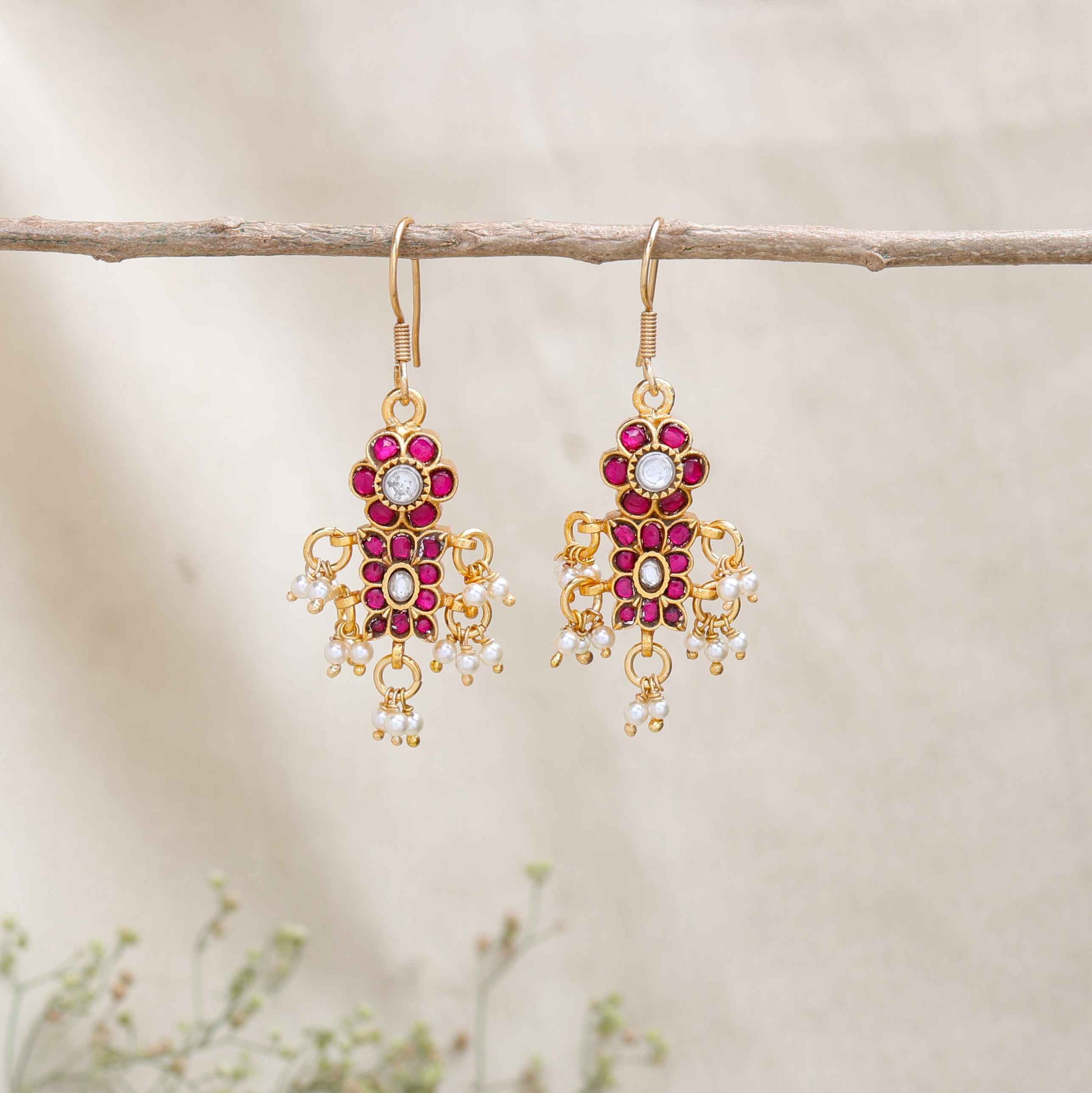 A close-up image of a woman's ear adorned with a gold-toned Kundan earring featuring pink and white gemstones in a floral design, with small pearl dangles adding movement and elegance.