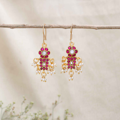 A close-up image of a woman's ear adorned with a gold-toned Kundan earring featuring pink and white gemstones in a floral design, with small pearl dangles adding movement and elegance.