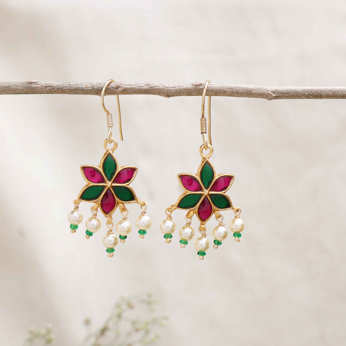 A gold-plated floral drop earring with pink and green enamel petals, featuring dangling freshwater pearls and green bead accents, worn by a model.