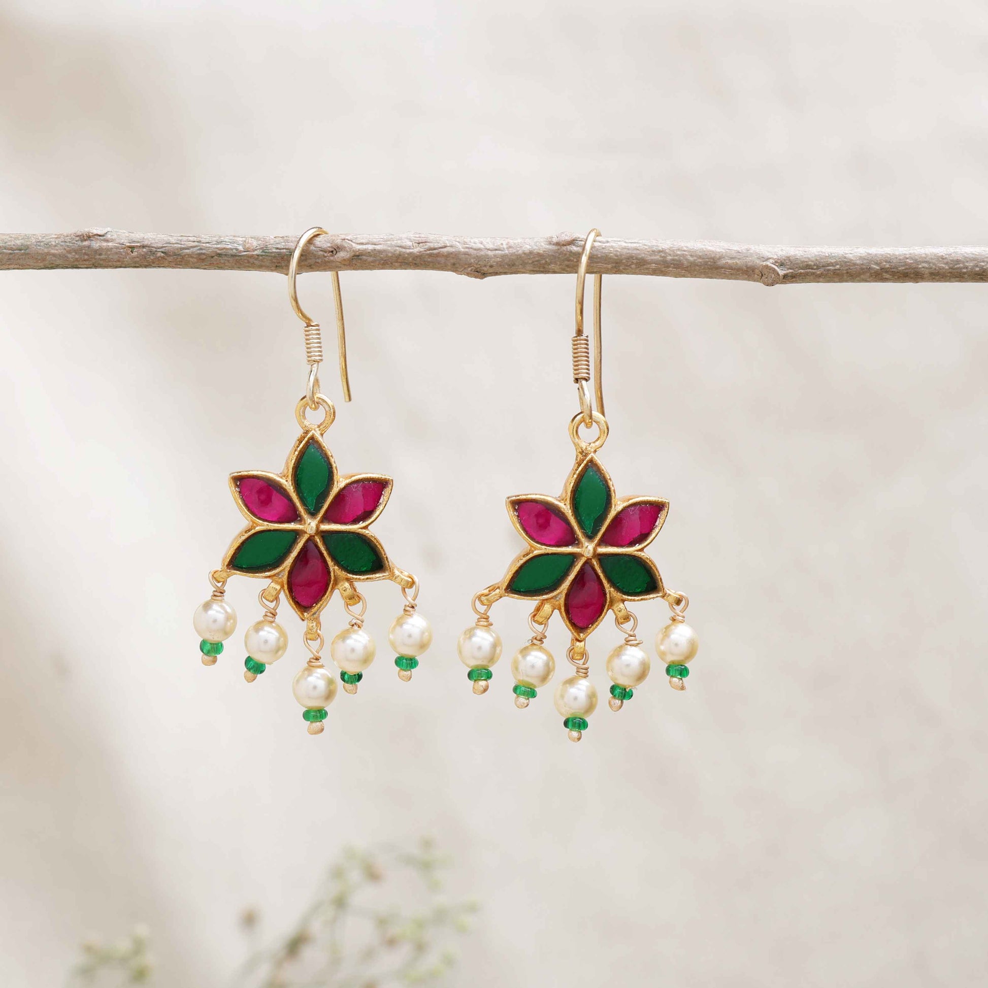 A gold-plated floral drop earring with pink and green enamel petals, featuring dangling freshwater pearls and green bead accents, worn by a model.