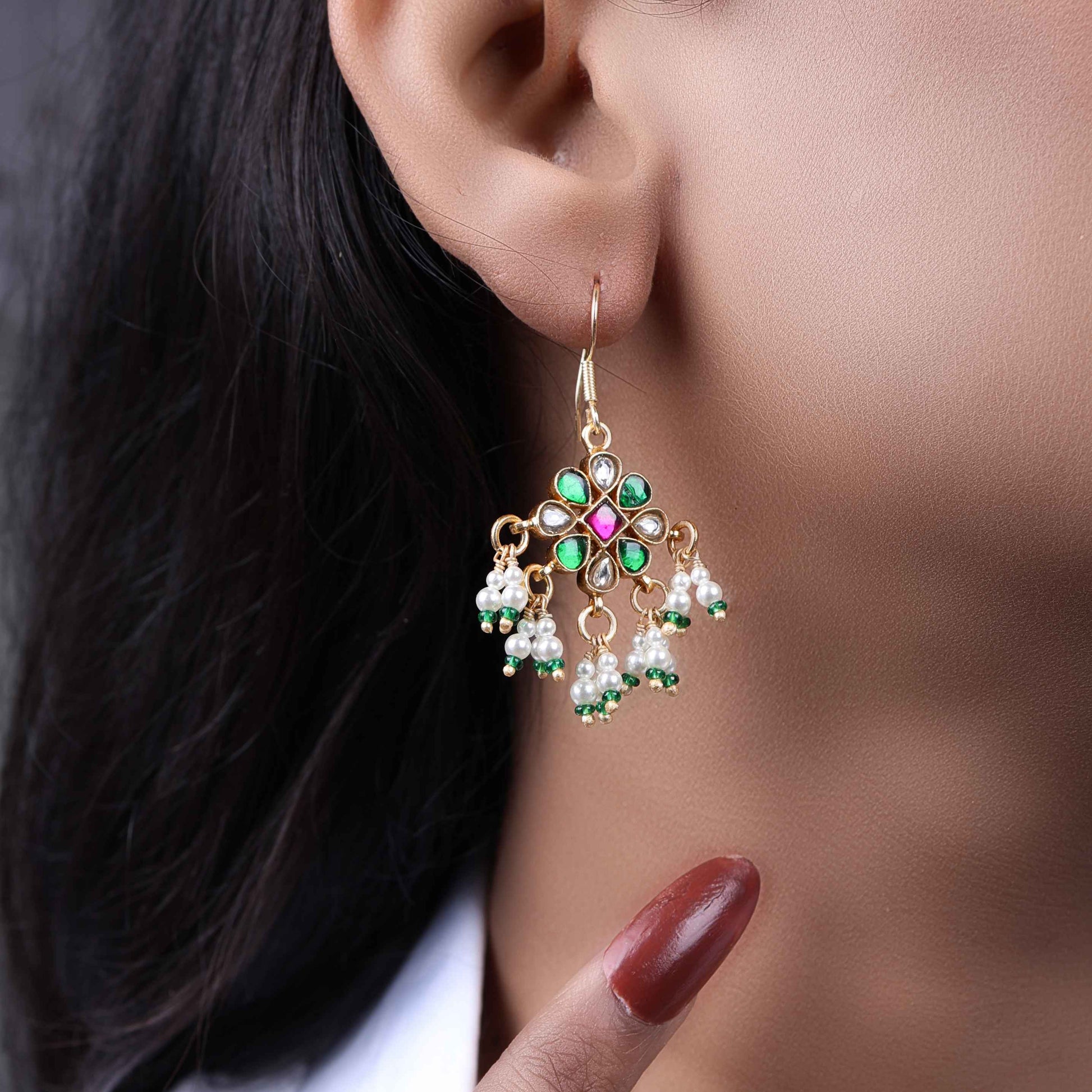 Gold-plated Kundan earrings with a floral motif, pink, green, and white gemstones, and dangling pearl clusters, worn by a model.