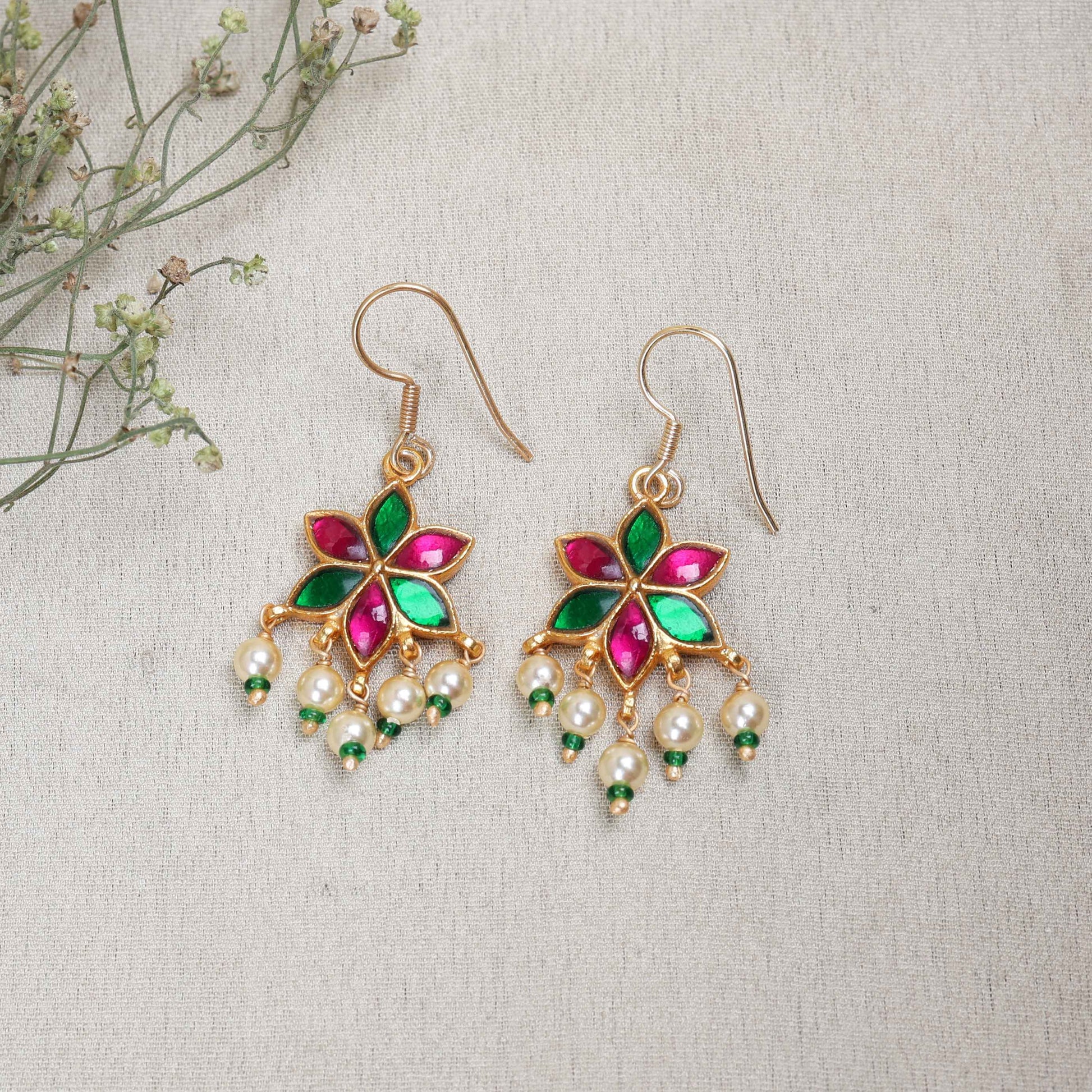 A gold-plated floral drop earring with pink and green enamel petals, featuring dangling freshwater pearls and green bead accents, worn by a model.