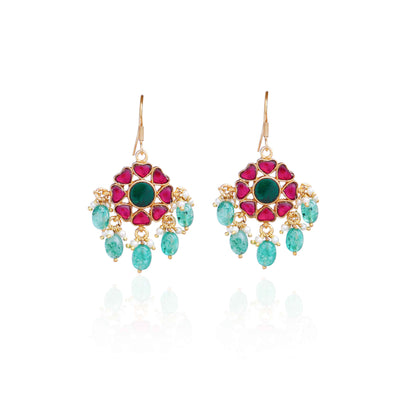Elegant gold-plated Kundan earrings with a floral design, featuring a central green gemstone, ruby-red stones, and dangling emerald-green beads and pearls, worn by a model.