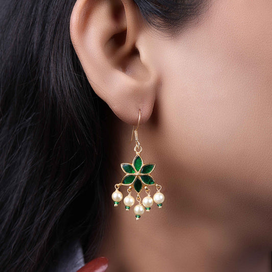 A close-up image of a woman's ear wearing a gold-toned drop earring with a green enamel floral design and five dangling pearls, creating an elegant and graceful look.