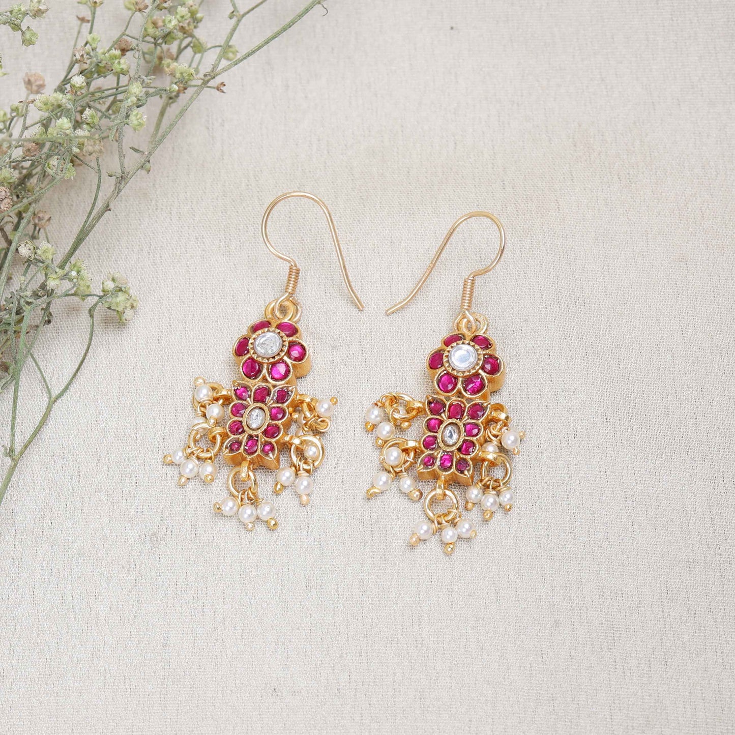 A close-up image of a woman's ear adorned with a gold-toned Kundan earring featuring pink and white gemstones in a floral design, with small pearl dangles adding movement and elegance.