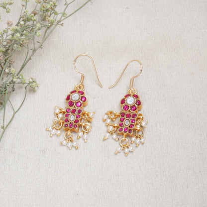 A close-up image of a woman's ear adorned with a gold-toned Kundan earring featuring pink and white gemstones in a floral design, with small pearl dangles adding movement and elegance.