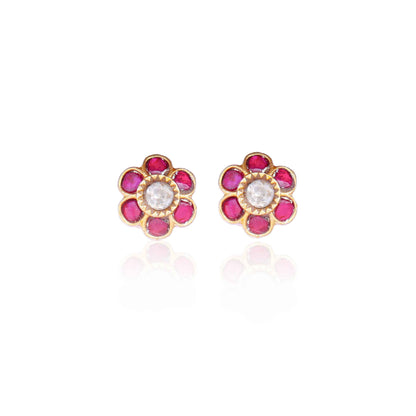 A close-up image of a woman's ear wearing a gold-toned floral stud earring, featuring a central white stone surrounded by pink gemstones, forming a flower shape.
