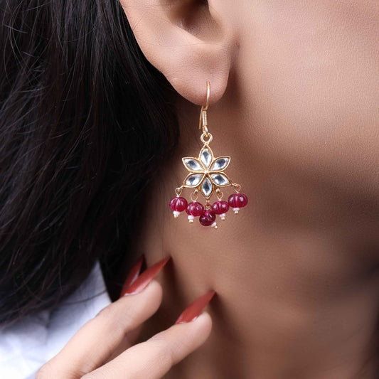 Gold-plated floral Kundan earrings featuring a six-petal design with clear gemstones and dangling red beads, elegantly worn by a model.
