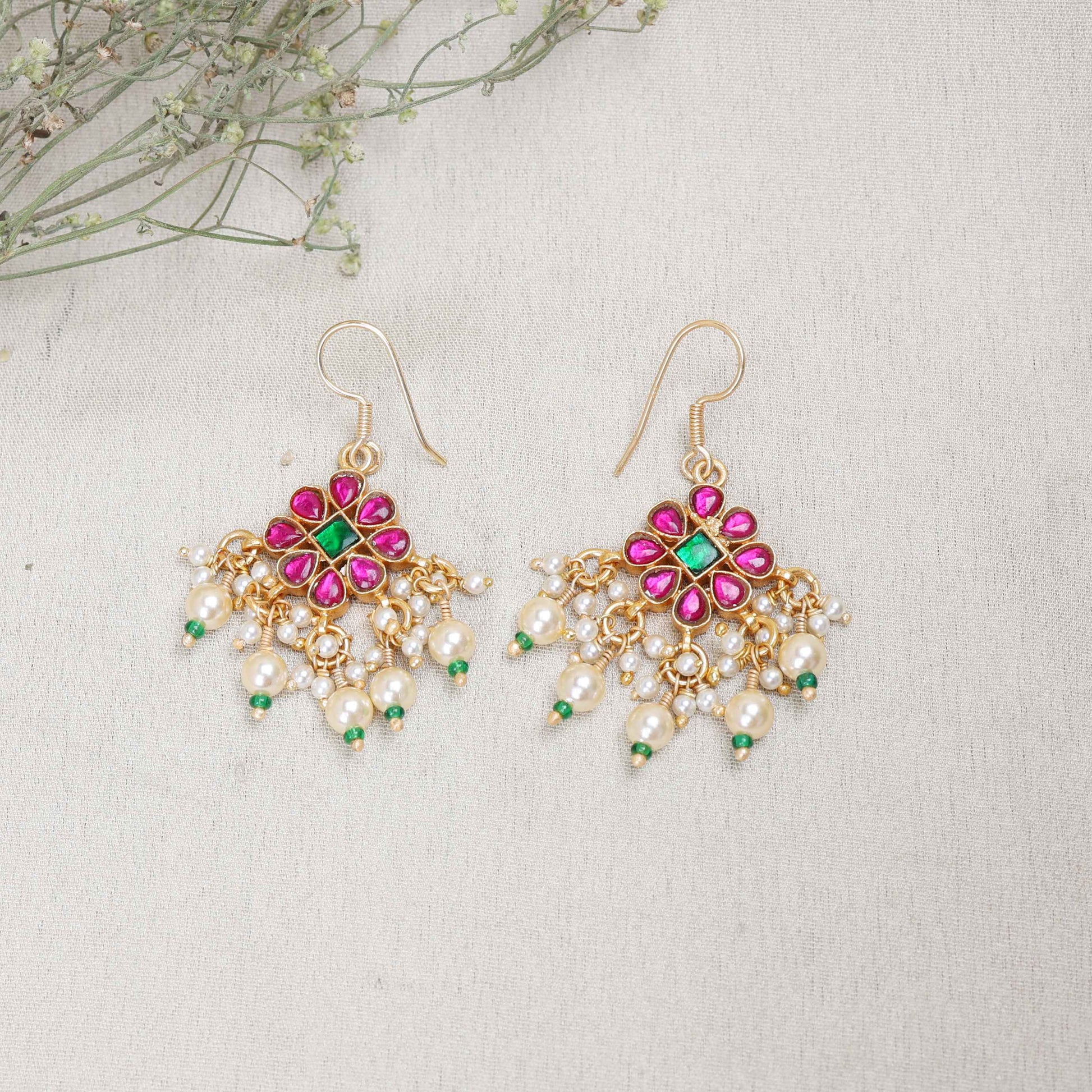 Gold-plated floral chandelier earrings with red and green gemstones, pearl drop accents, and intricate detailing, perfect for ethnic and festive wear.