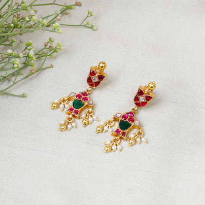 Gold-plated Kundan earrings with red and green gemstones, intricate floral design, and dangling pearl drops, perfect for traditional and festive wear.