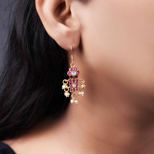 A close-up image of a woman's ear adorned with a gold-toned Kundan earring featuring pink and white gemstones in a floral design, with small pearl dangles adding movement and elegance.