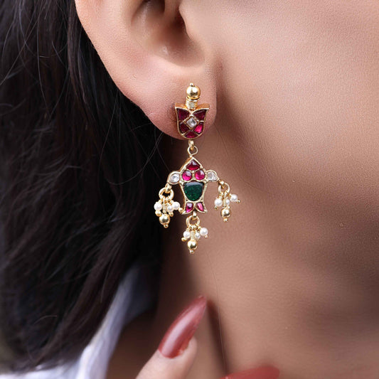 Gold-plated Kundan earrings with red and green gemstones, intricate floral design, and dangling pearl drops, perfect for traditional and festive wear.