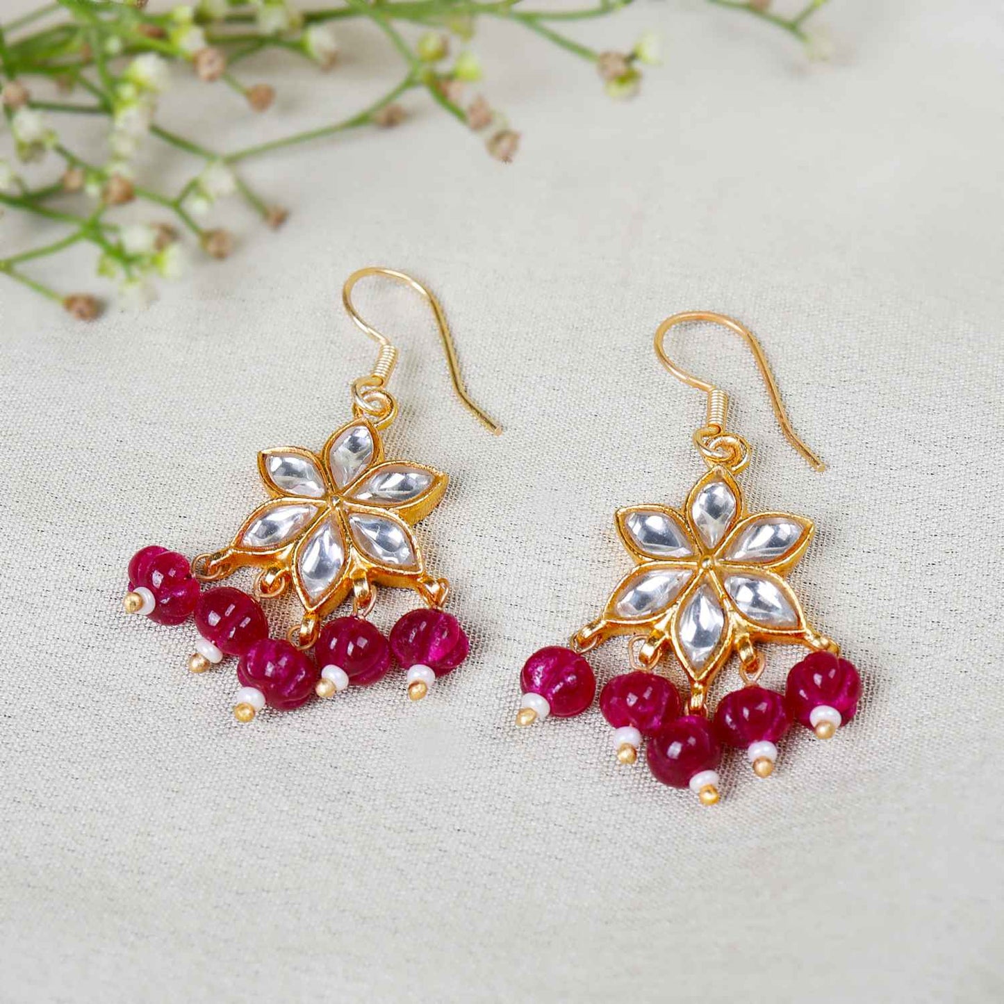 Gold-plated floral Kundan earrings featuring a six-petal design with clear gemstones and dangling red beads, elegantly worn by a model.