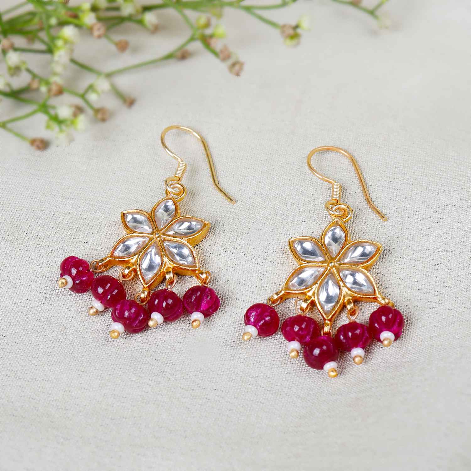 Gold-plated floral Kundan earrings featuring a six-petal design with clear gemstones and dangling red beads, elegantly worn by a model.