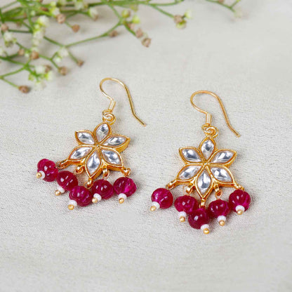 Gold-plated floral Kundan earrings featuring a six-petal design with clear gemstones and dangling red beads, elegantly worn by a model.