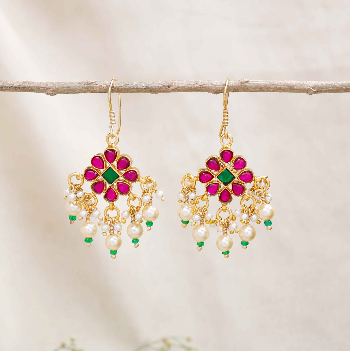 Gold-plated floral chandelier earrings with red and green gemstones, pearl drop accents, and intricate detailing, perfect for ethnic and festive wear.
