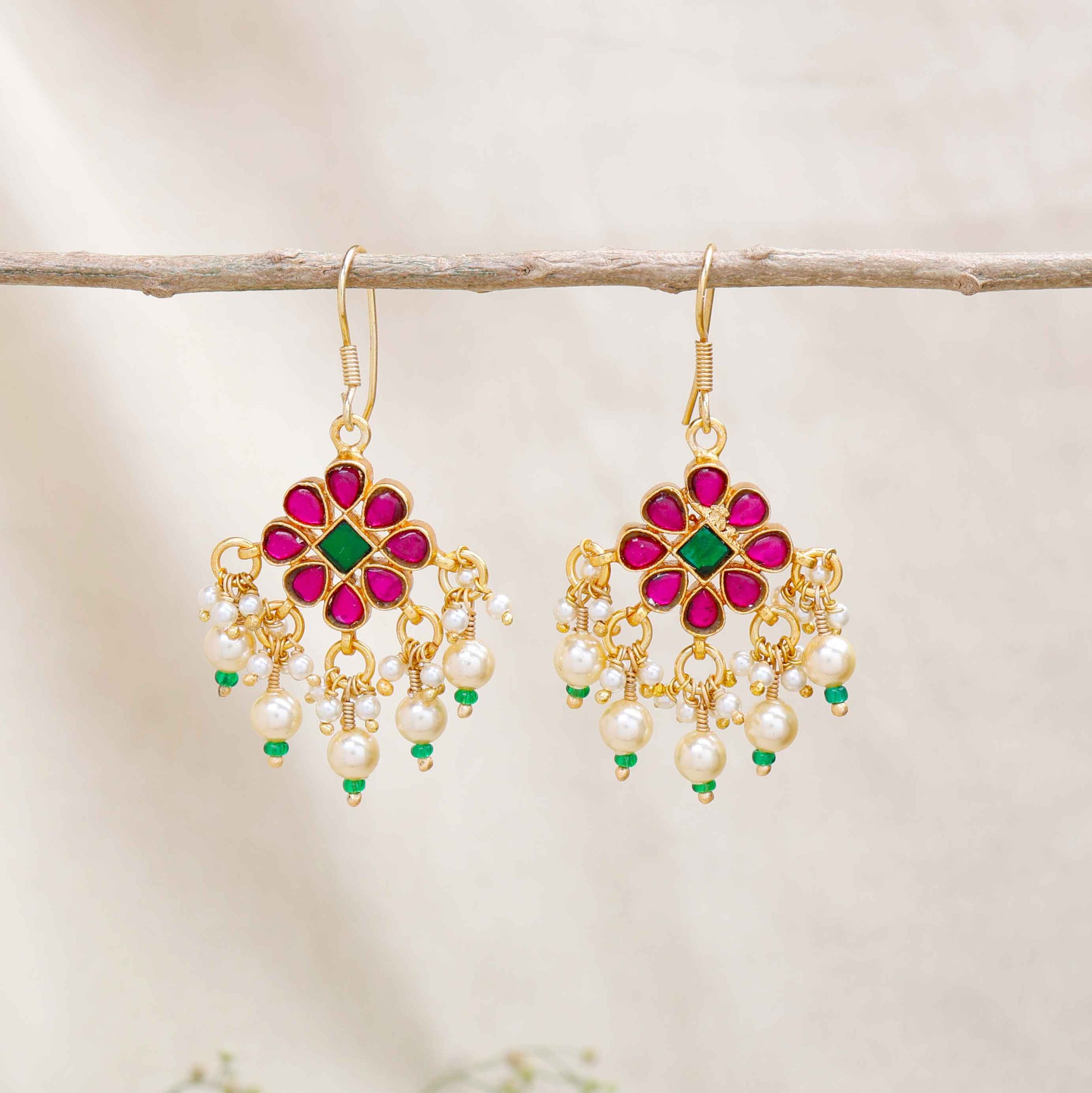 Gold-plated floral chandelier earrings with red and green gemstones, pearl drop accents, and intricate detailing, perfect for ethnic and festive wear.