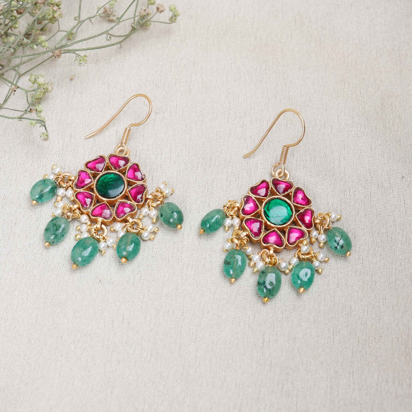 Elegant gold-plated Kundan earrings with a floral design, featuring a central green gemstone, ruby-red stones, and dangling emerald-green beads and pearls, worn by a model.