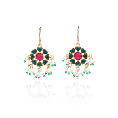 A gold-plated floral Kundan earring with a ruby-red center stone, deep green enamel petals, and dangling freshwater pearls, worn by a model with elegant styling.